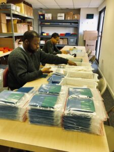 Two young men sitting at a table assembling products