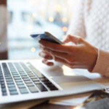 Hands holding a phone while using a laptop