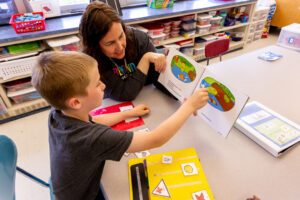 A teacher reads a book with a young student