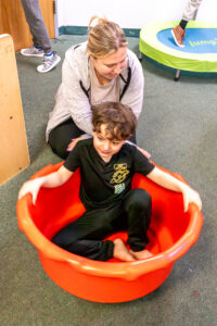 A young student is sitting in a large red tub for sensory play
