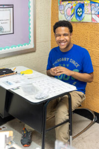 A smiling high school student is seated at a desk